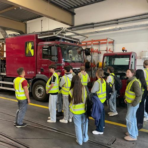 Jugendliche in Warnwesten besichtigen Feuerwehrfahrzeuge in einer Fahrzeughalle